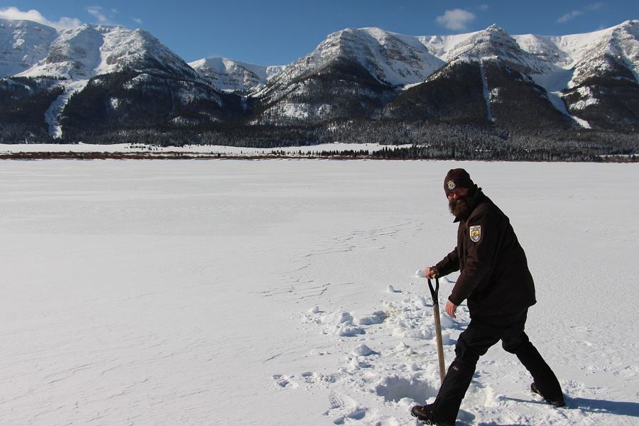 Angler cranking a hand auger on a snowy frozen lake