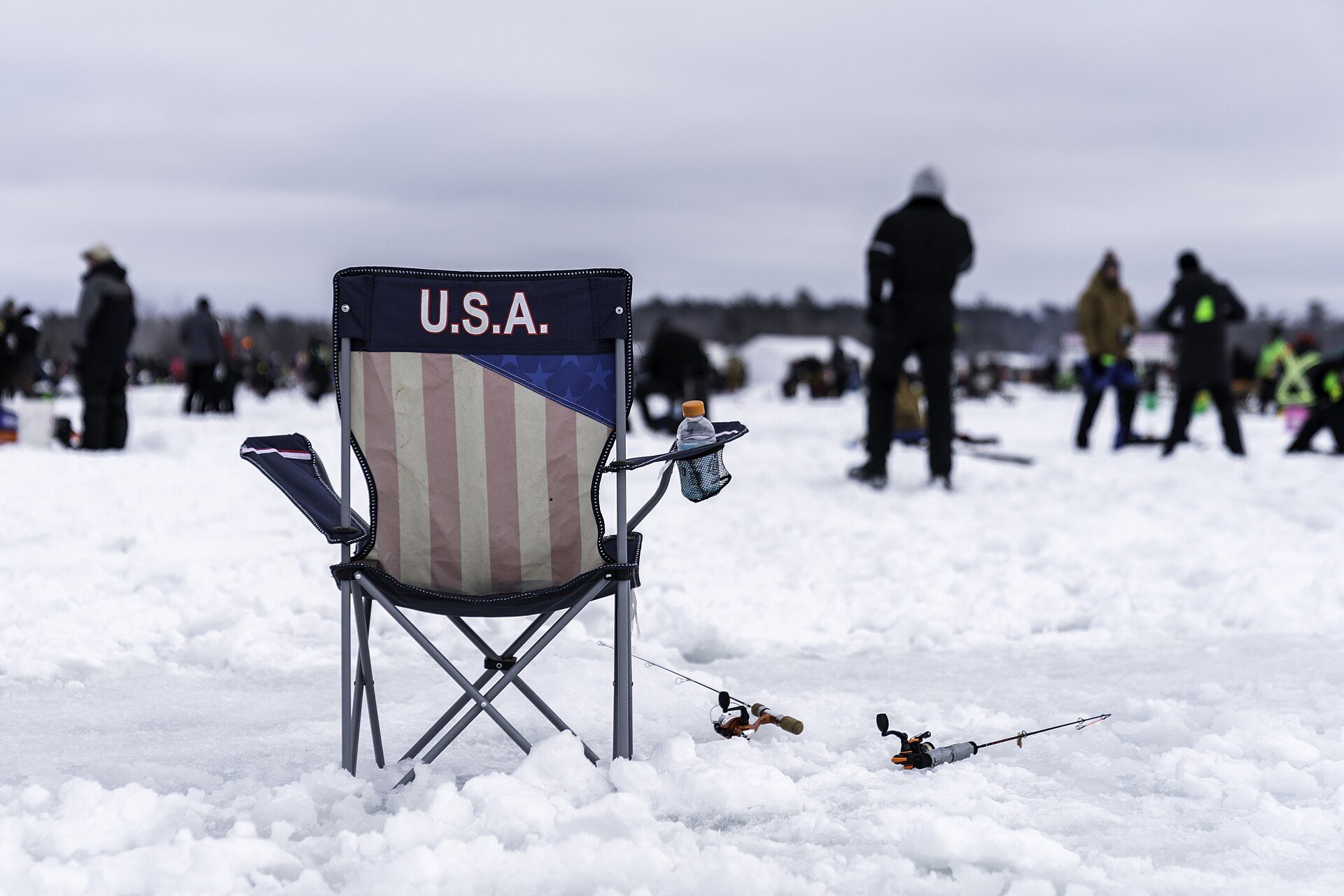 Camp chair and short ice rods set beside holes on a snowy frozen lake