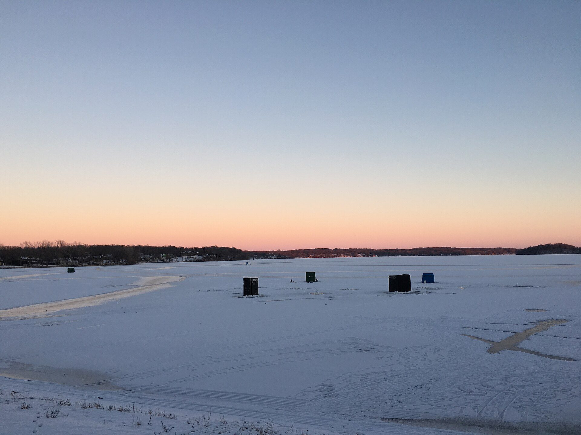 Ice fishing houses dotting a frozen lake at dusk