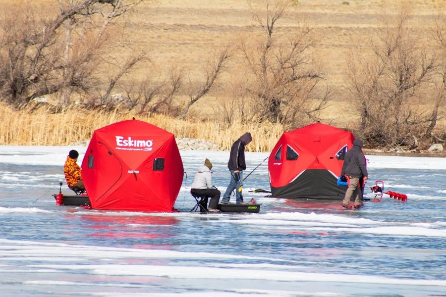 Two red pop-up hub shelters set up on lake ice with anglers fishing nearby