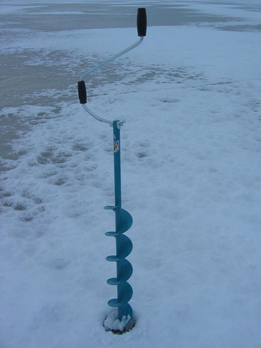 Hand auger standing in a fresh hole drilled through snow-covered ice