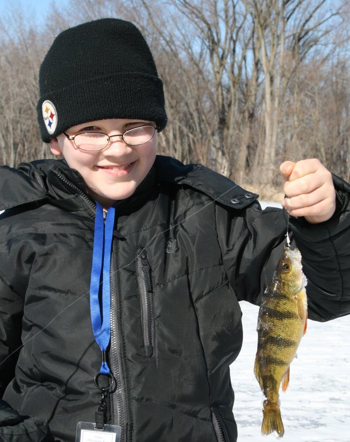 Young angler on a frozen lake holding up a yellow perch caught through the ice
