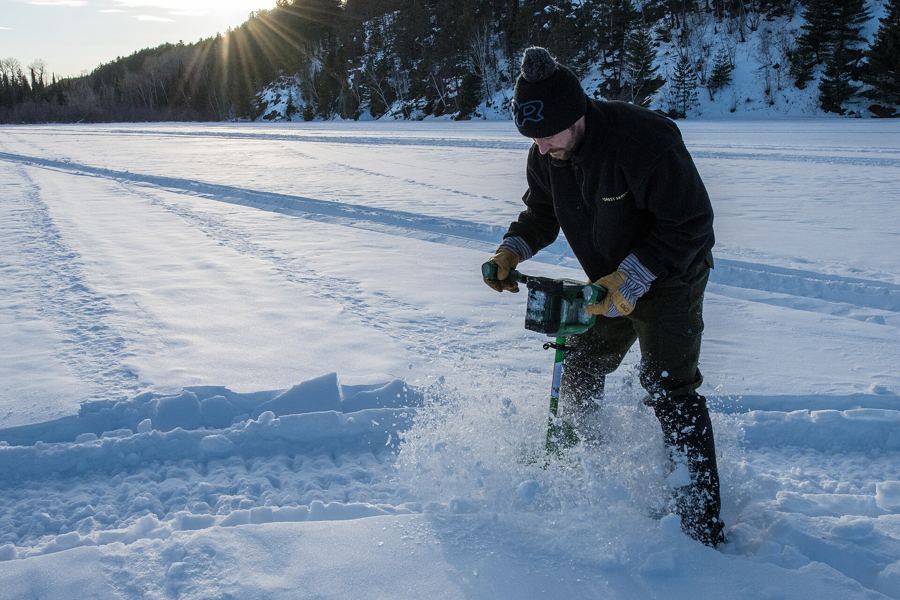Angler drilling through lake ice with a power auger on a sunny winter day