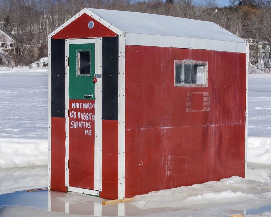 Red wooden ice fishing shack on a snow-covered lake
